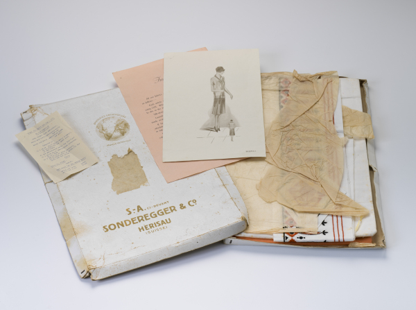Contents of the Sonderegger & Co dress kit, including box, fabric wrapped in tissue, fashion illustration, washing instructions and list of contents.